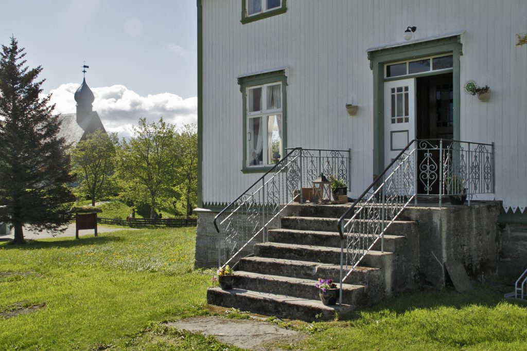 Inngangsparti med trapp inn Dønnes Gård. I bakgrunnen til venstre mellom trær står Dønnes kirke.