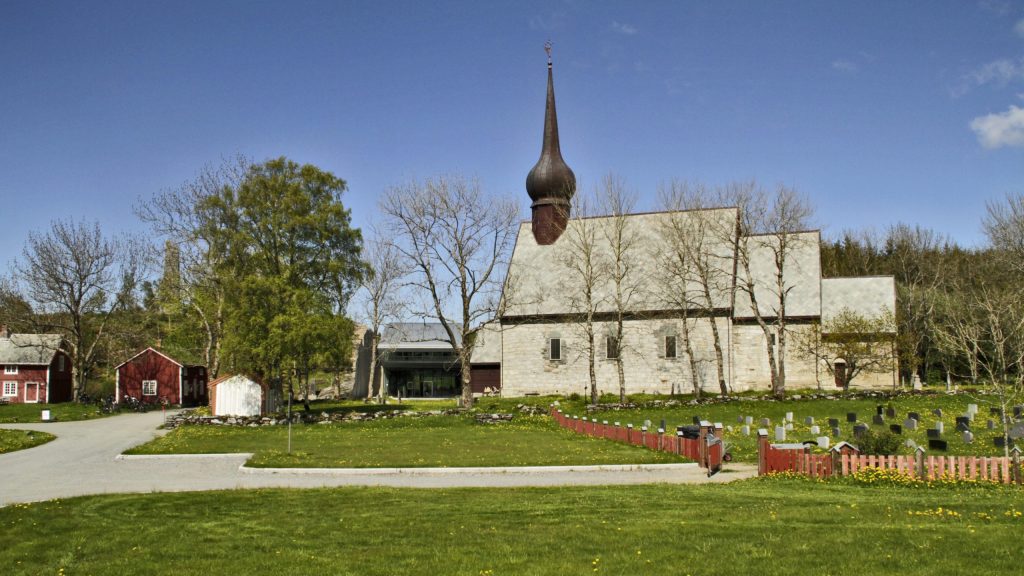 Middelalderkirken og det moderne Petter Dass-museet på Alstahaug-tunet med kirkegården til høyre og historiske røde byggene på tunet til venstre