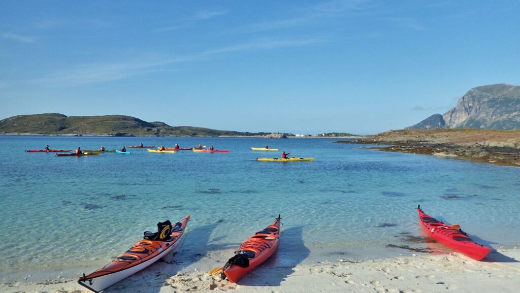 Kajakker på sandtrand med padlere på vannet utenfor