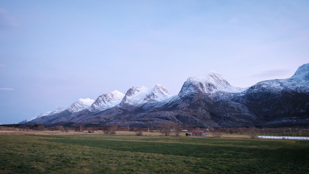 Fjellkjeden De Syv Søstre ved solnedgang. I forgrunnen er det åkerland med trær, høyballer og et gammelt uthus.