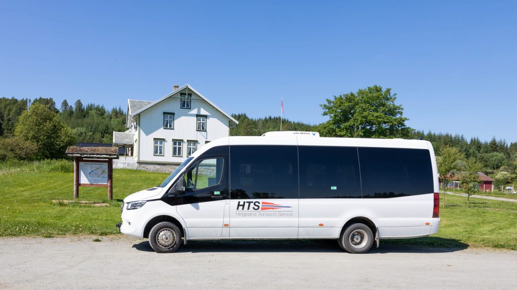 Hvite gårdshuset på Dønnes Gård står bak HTS sin minibuss på parkeringsplassen en sommerdag