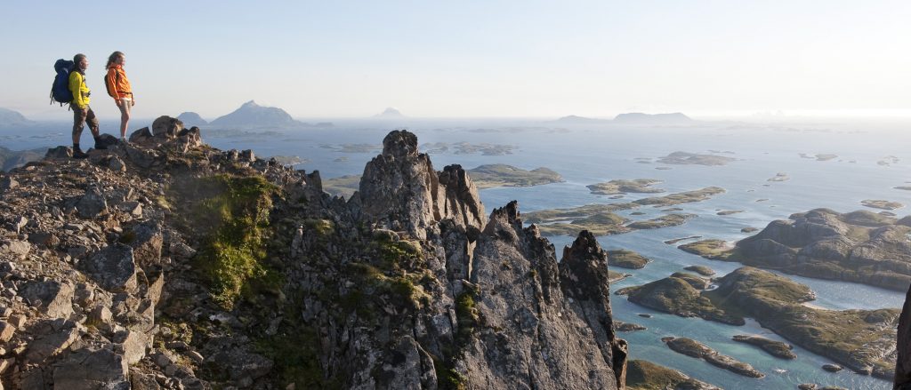 En mann og kvinne i sportstøy på fjelltur på Rødøyløva i Rødøy. I bakgrunnen ser vi Hestmannen og mange andre øyer og holmer i skjærgården rundt Rødøya