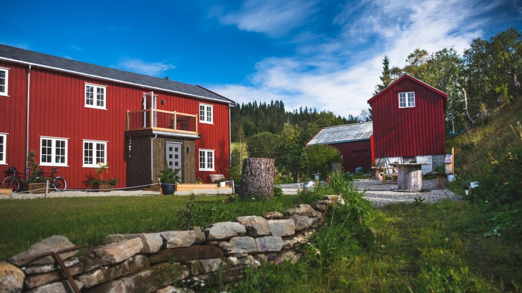 Røde bygninger med grønt gressplen foran og skog i bakgrunn