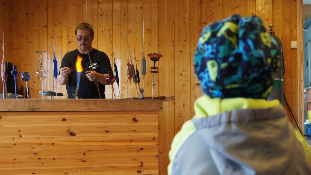 Mann står å holder glass over en flamme mens barn sitter å ser på