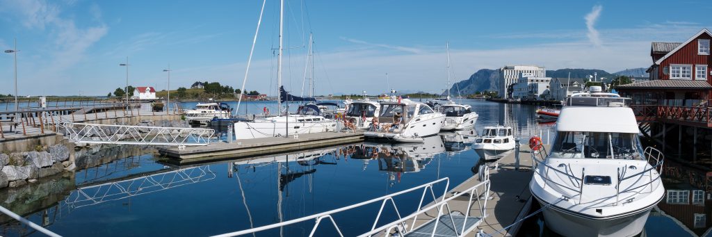 Bilde av gjestehavna i Brønnøysund en solskinnsdag om sommeren. Det er mange båter i havna, og i og ved noen av dem sitter båtfolk og soler seg i sommervarmen.