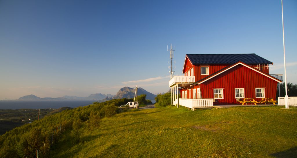 Dønnesfjellstua i solskinn til høyre på bakketoppen med utsikt til Nesnaøyene og Lurøy i nord, til venstre forbi Dønnafjellstua