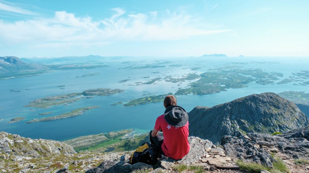 Person on a mountain hike at the top of the mountain Dønnamannen on Dønna with a view of the Helgeland coast on a beautiful summer day