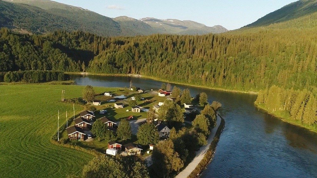 Korgen Camping med elva Røssåga rennende rundt. Skog og fjell i bakgrunn.