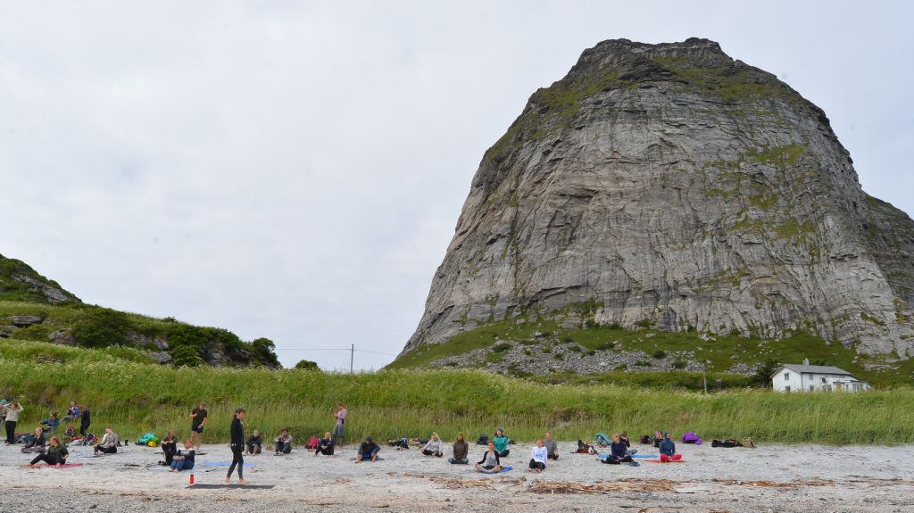 Gruppe som utfører yoga på sandstrand med fjellet Trænstaven i bakgrunn