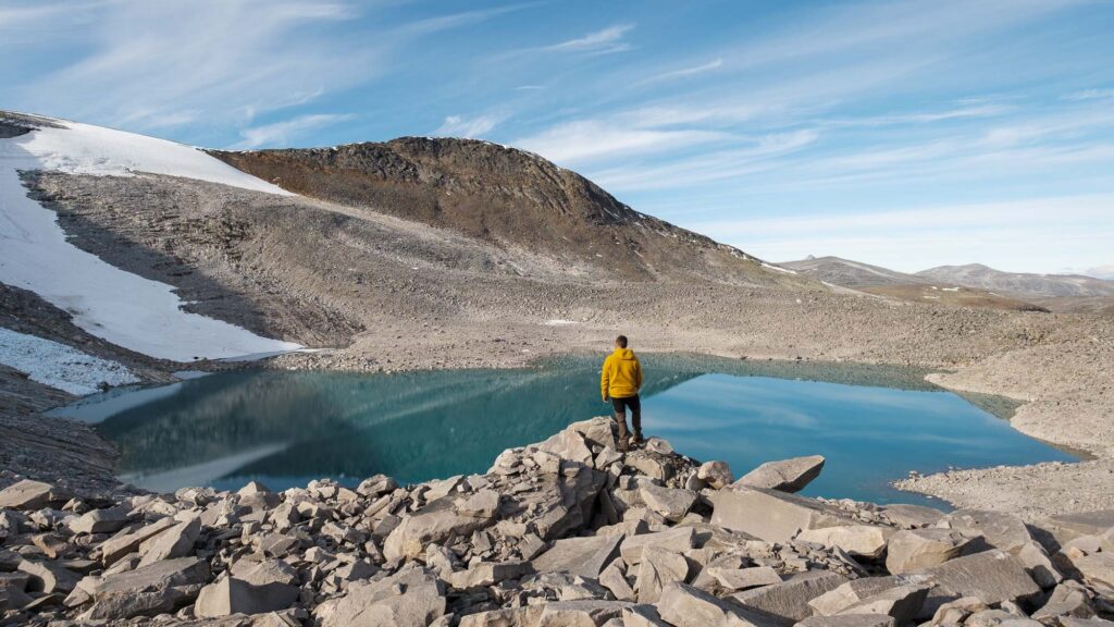 En turgåer står foran et brevann ved en liten isbre høyt i Saltfjellet
