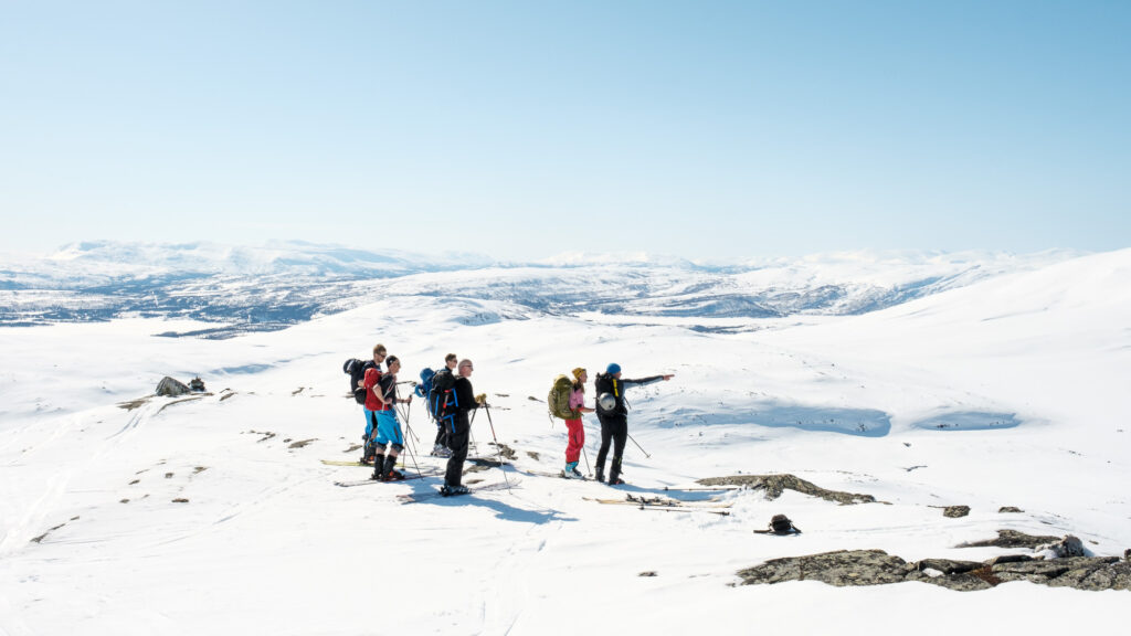 Turgruppe med seks voksne og guide på topptur høyt oppe i vinterfjellet en finværsdag rundt påsketider