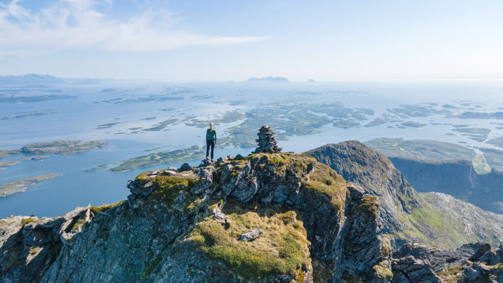 Person på fjelltur på toppen av fjellet Dønnamannen på Dønna med utsikt over Helgelandskysten en vakker sommerdag