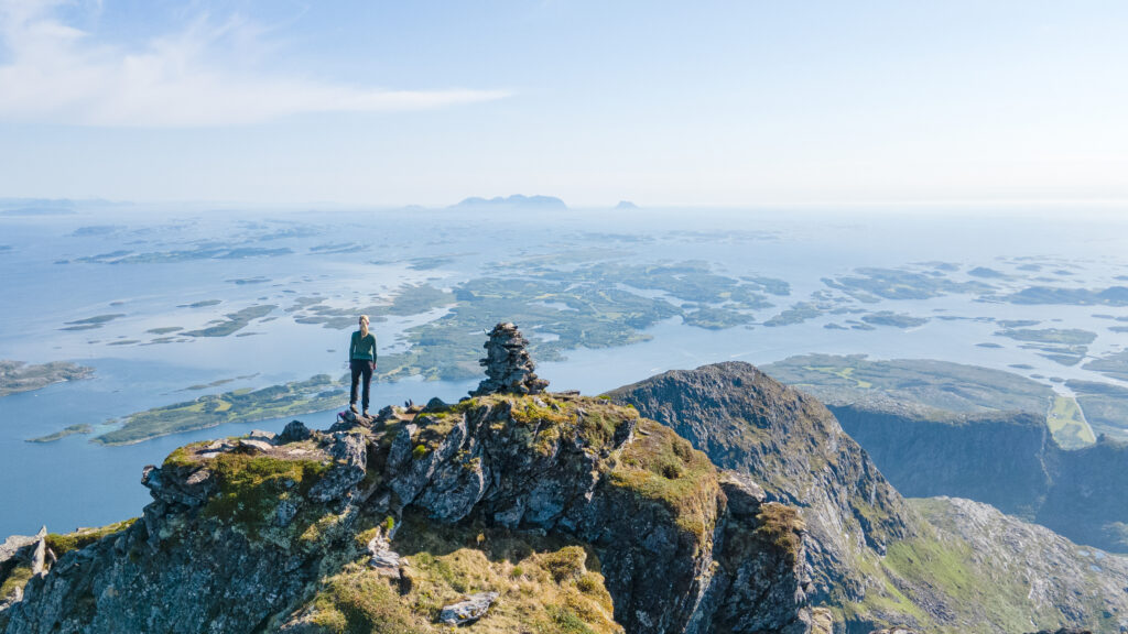 Person på fjelltur på toppen av fjellet Dønnamannen på Dønna med utsikt over Helgelandskysten en vakker sommerdag