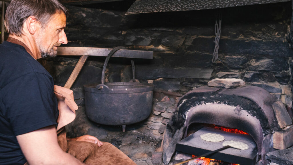 En mann steker tradisjonsbaksten kamkake i vedfyrt ovn.