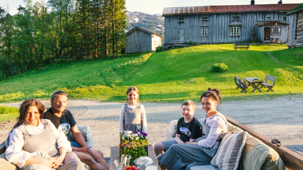 Vertskapet 3 voksne og 2 barn foran gammelstua i Inderdalen