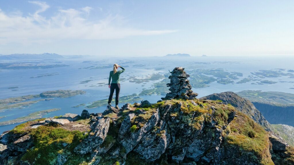 Person on a mountain hike at the top of the mountain Dønnamannen on Dønna with a view of the Helgeland coast on a beautiful summer day