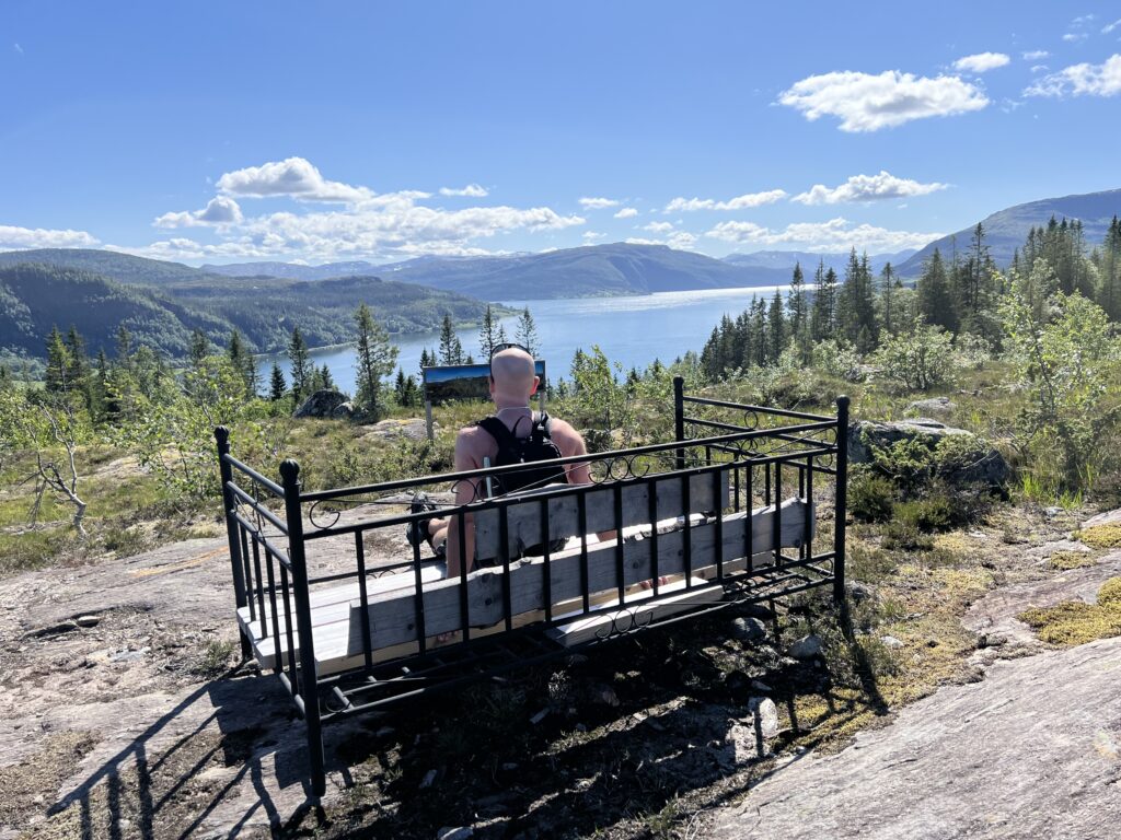 En mann som sitter på en benk og ser utover fjord og fjell