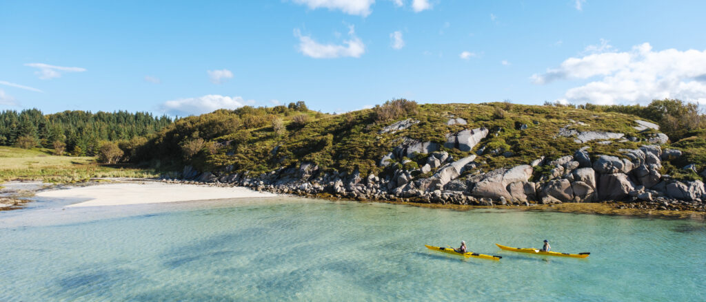 To kajakkpadlere på tur i kajakk ved øya Kvarøy og Hestmannen på Helgelandskysten en fin sommerdag