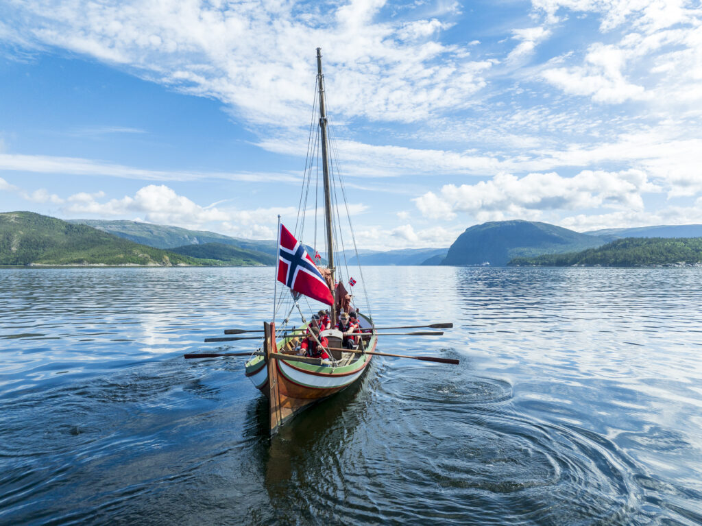Nordlandsbåt på fjorden med norske flagg.