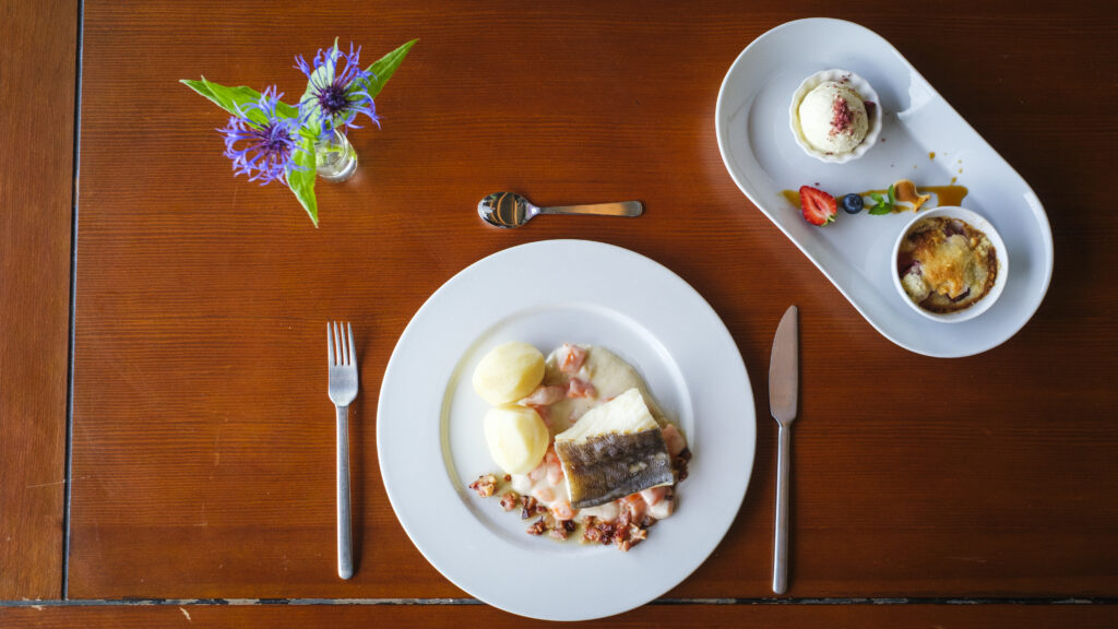 To tallerkener med mat på et bord. Den ene med boknafisk og tilbehør. Den andre med dessert.
