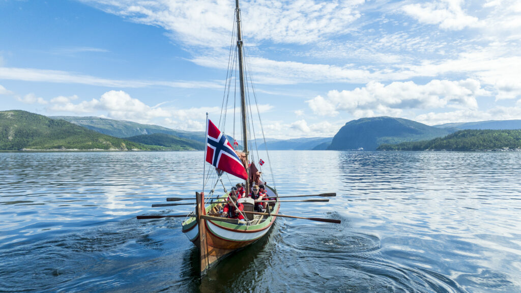 Nordlandsbåt på fjorden med norske flagg.